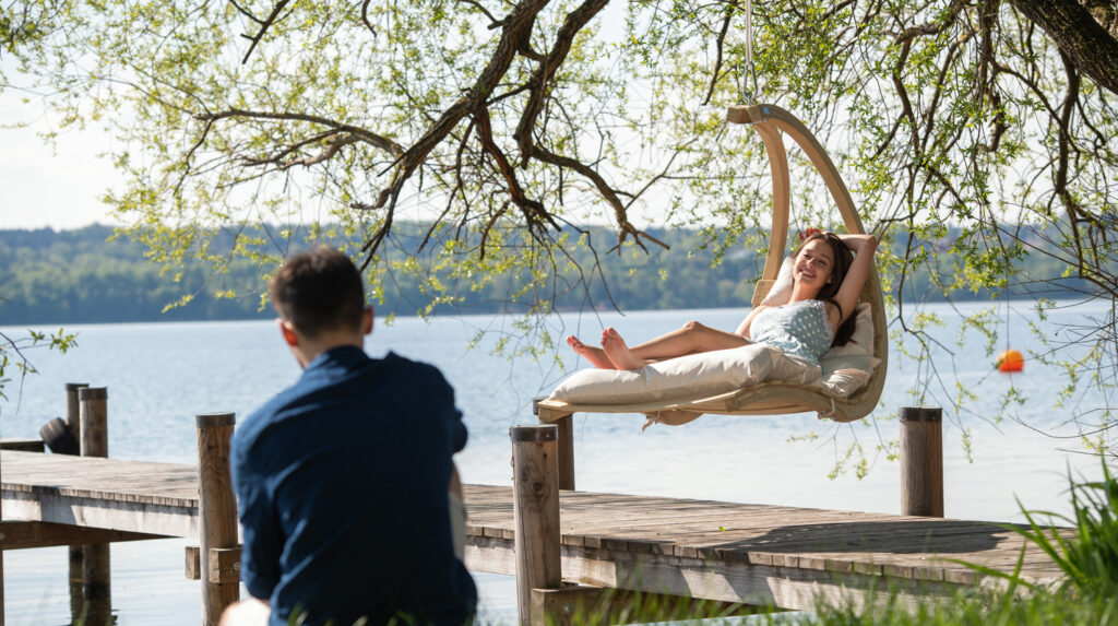 Eine Frau sitzt in einem Hängesessel an einem Steg an einem See